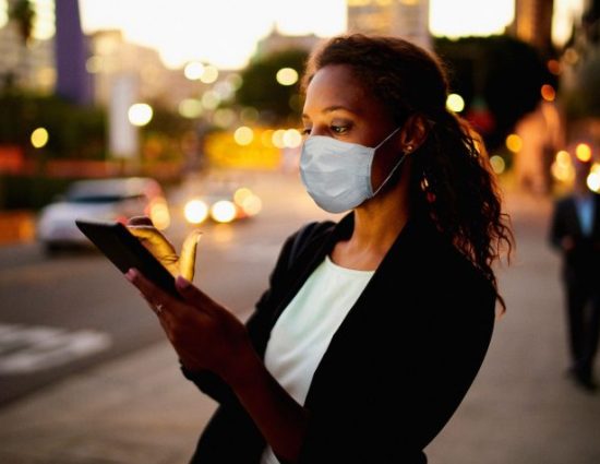 Businesswoman using a digital tablet at night in the city wearing a face mask.