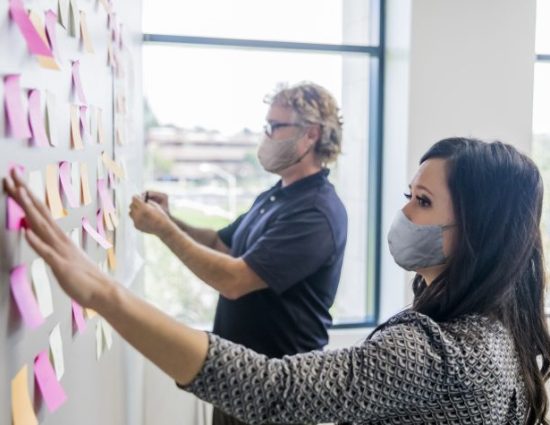 Two people leading a brainstorming session by putting post it notes on the wall