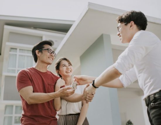 Smiling couple collecting house keys from real estate agent after buying a house