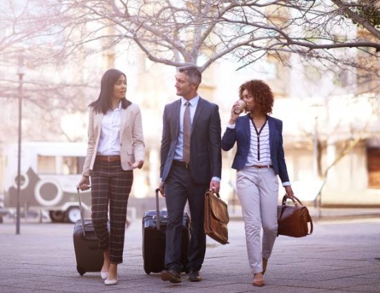 3 business people walking and talking to each other while carrying their luggage outside