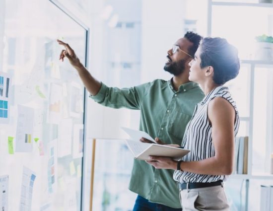 Shot of two businesspeople brainstorming with notes on a glass wall in an office