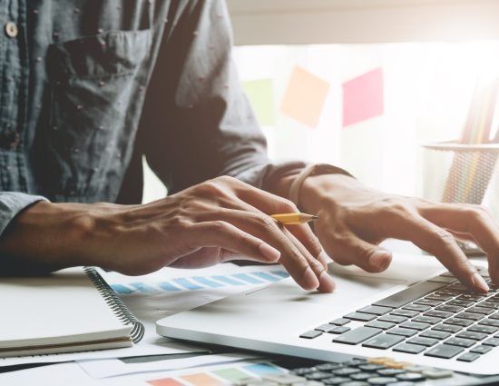 Close up of businessman or accountant hand holding pen working on laptop computer for calculate business data, accountancy document and calculator at office