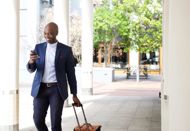 businessman in suit walking with a suitcase outside of a business building